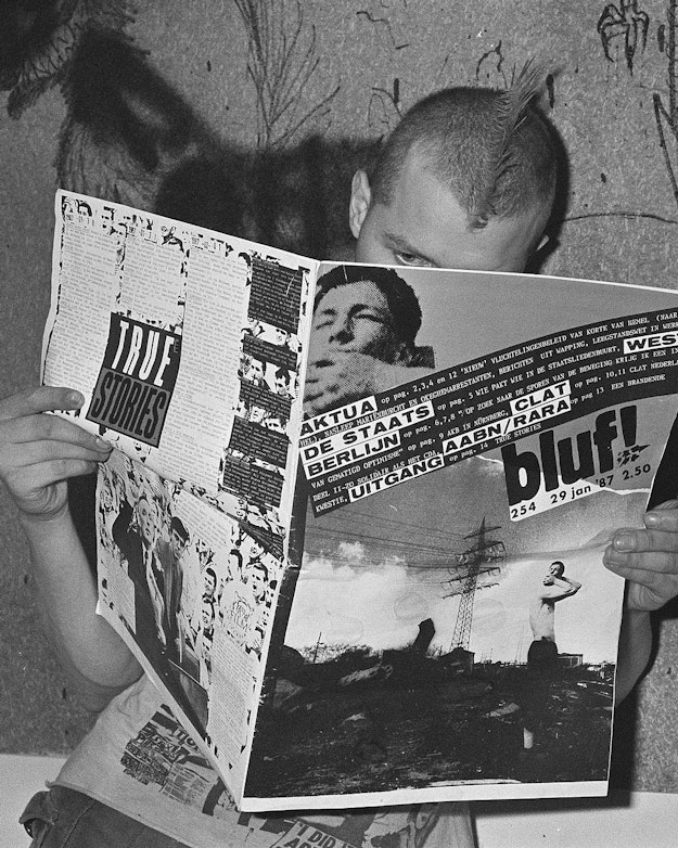 Man met hanenkam houdt opengeslagen krant voor zich (zwart-witfoto).