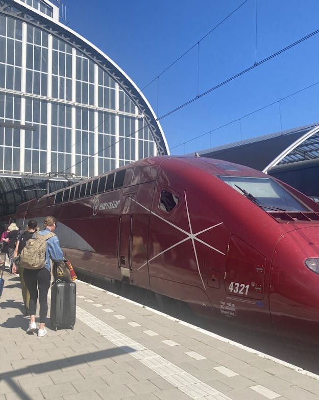 De hogesnelheidstrein naar Parijs op station Amsterdam Centraal. De kop van een bordeauxrode hogesnelheidstrein staat buiten een station naast het perron. Op het perron lopen reizigers met koffers.