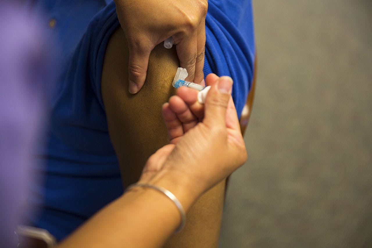 Iemand krijgt een vaccin tegen de griep in zijn arm gespoten.