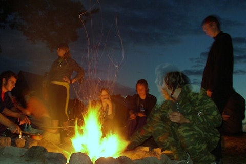 Een groep mensen zit 's nachts rond een kampvuur.
