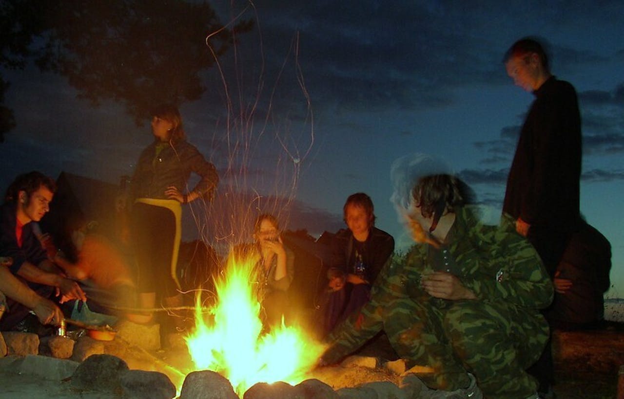 Een groep mensen zit 's nachts rond een kampvuur.