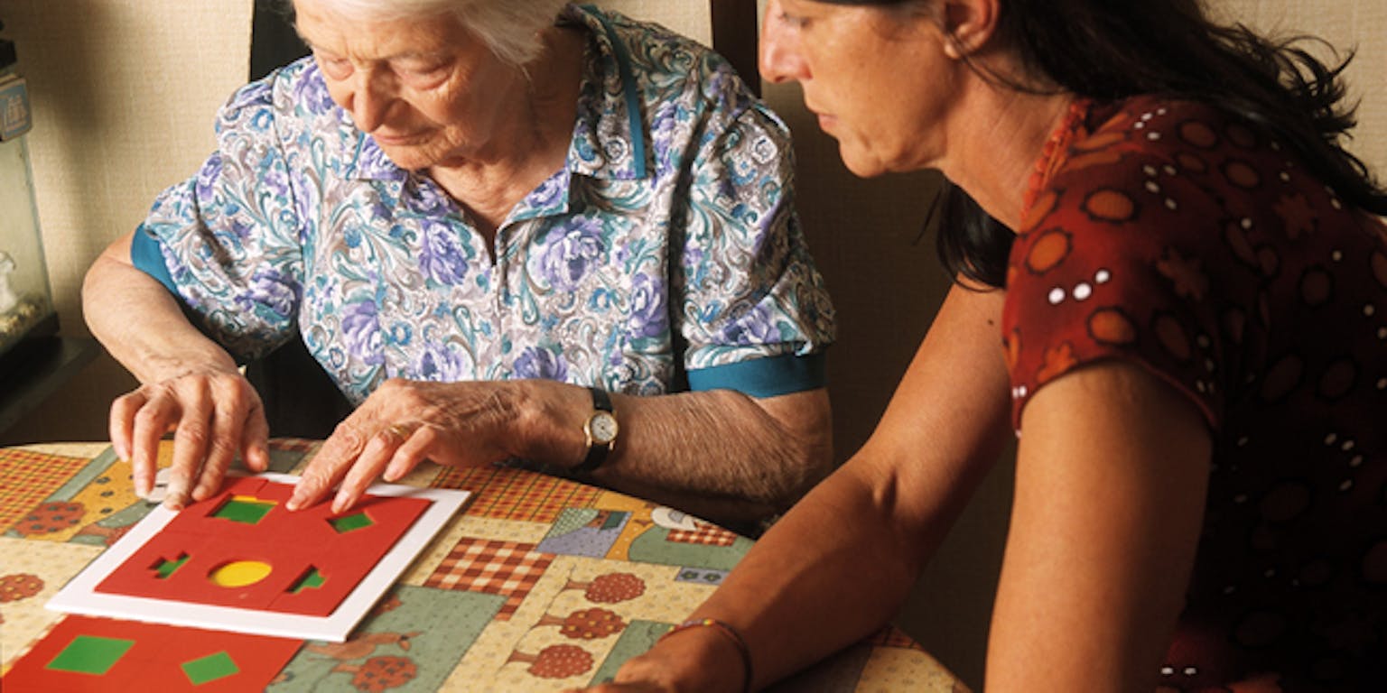 Een persoon doet samen met een oudere dame aan tafle een geheugentest spel.