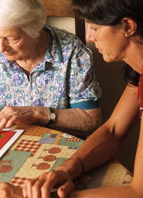 Een persoon doet samen met een oudere dame aan tafle een geheugentest spel.