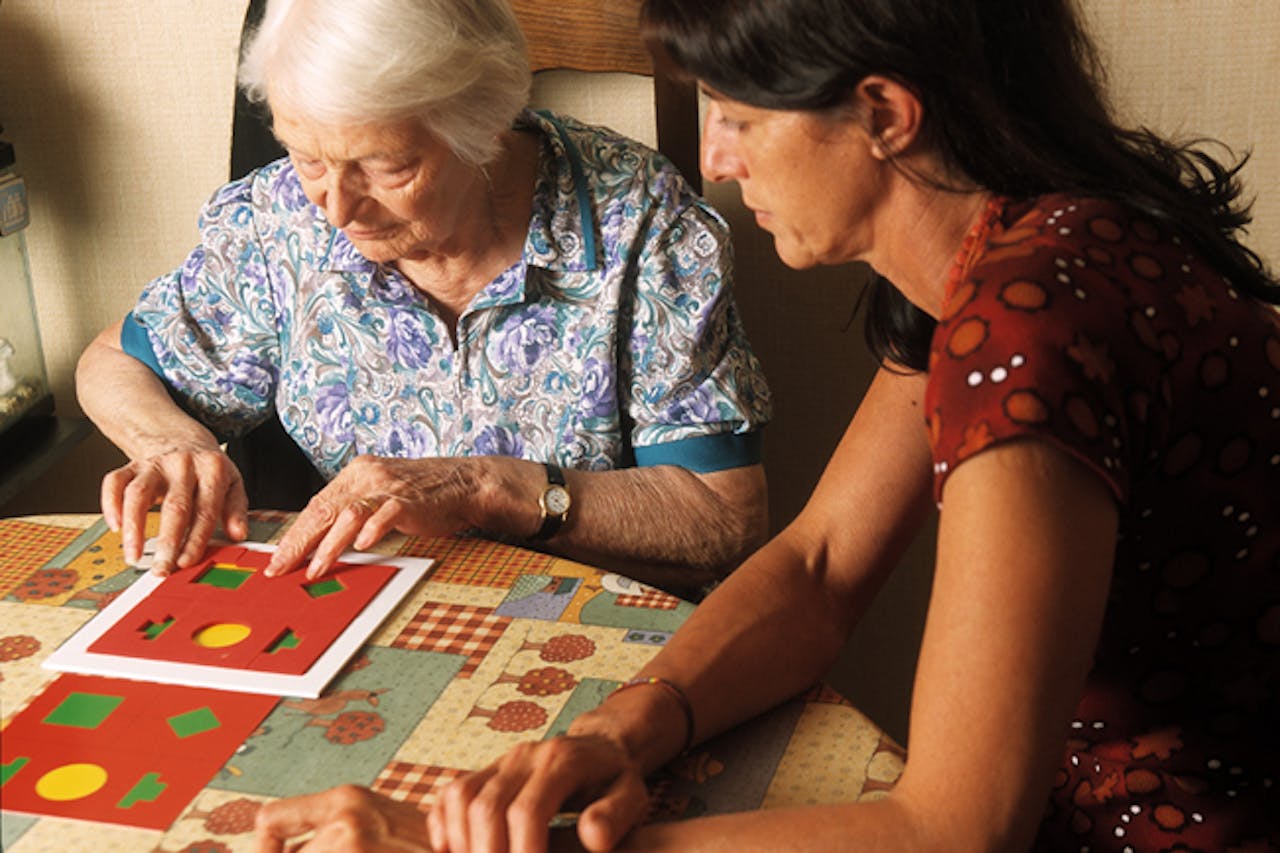 Een persoon doet samen met een oudere dame aan tafle een geheugentest spel.