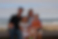 Een foto van een gezin die poseert voor de foto. Het gezin zit op een bankje bij het strand.