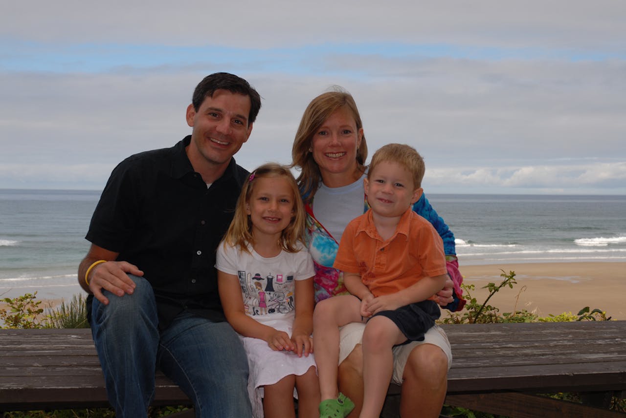 Een foto van een gezin die poseert voor de foto. Het gezin zit op een bankje bij het strand.