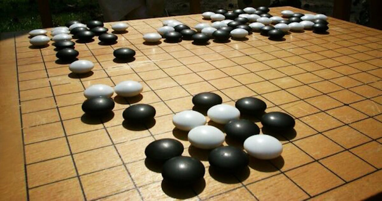 Het spelbord van GO: een houten bord verdeeld in vierkanten met daarop witten en zwarte stenen.