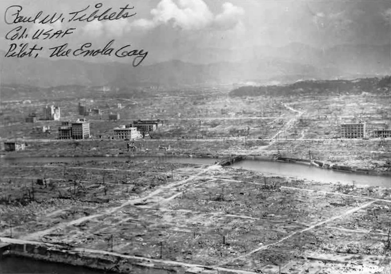 Een zwart-wit foto van Hiroshima, na de atoombom. Op de foto is een handschrift van de piloot Paul Tibbets te lezen.