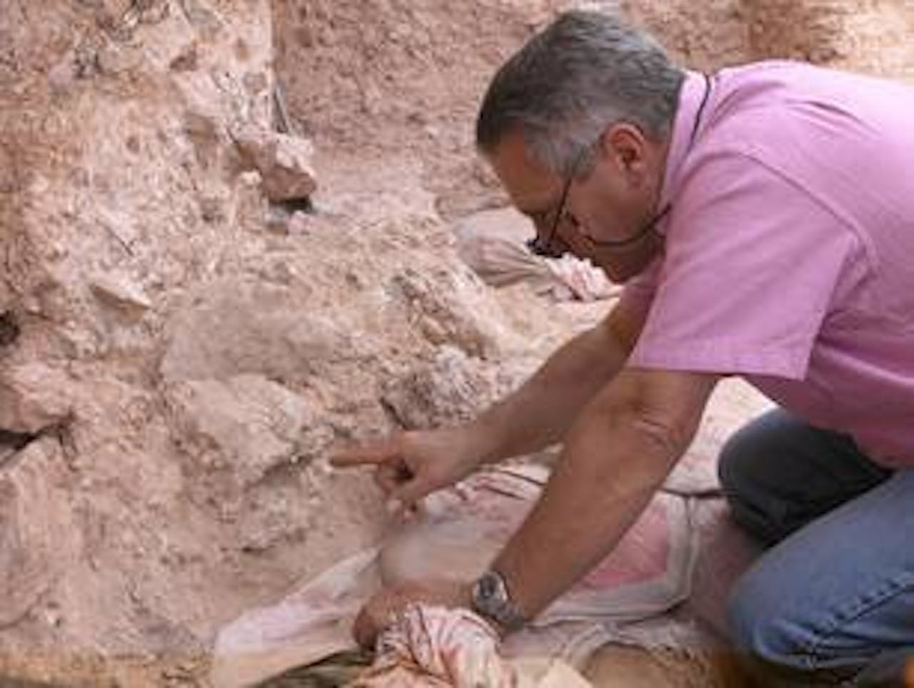 Jean-Jacques Hublin op de archeologische opgravingslocatie Jebel Irhoud (Marokko). Hij wijst naar het fossiel van een schedel, waarvan de oogkassen zichtbaar zijn.
