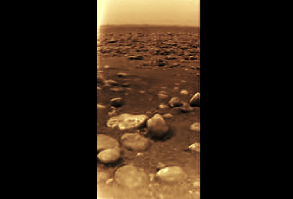 <p>Een foto van het oppervlak van de grootste Saturnusmaan Titan, gemaakt door de Huygens-sonde die er begin 2005 landde. Door de dikke atmosfeer van voornamelijk stikstof is een vaste ondergrond zichtbaar, met waarschijnlijk ‘stenen’ van waterijs van ongeveer tien tot vijftien centimeter groot. De temperatuur op de landingsplaats was -180 graden Celsius. Ook is het er donker: in vergelijking met de aarde is de lichtsterkte ongeveer duizend maal zwakker, vergelijkbaar met een diepe schemering.</p>