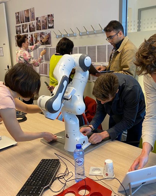 Oncologieverpleegkundigen ontdekken tijdens een workshop de mogelijkheden van een robotarm. Op een tafel staat een robotarm. Mensen eromheen ontdekken de mogelijkheden.