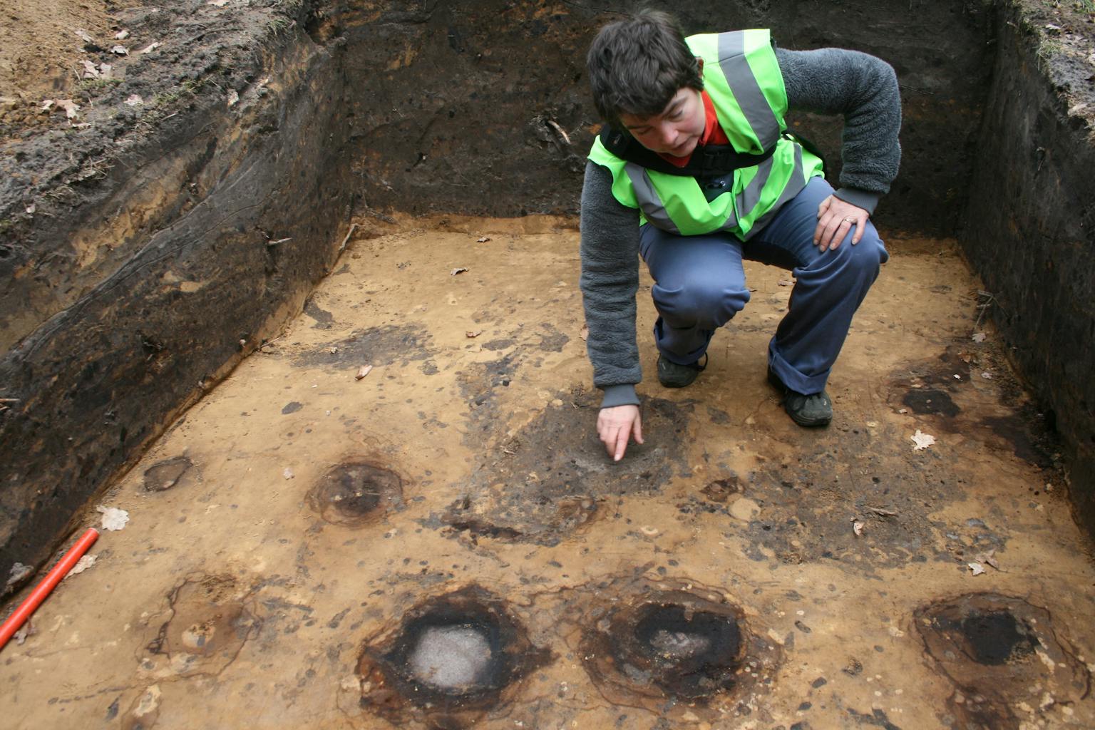 Liesbeth Theunissen wijst in een werkput de sporen aan (bruin met grijze binnenkern) van twee palen uit de bronstijd.