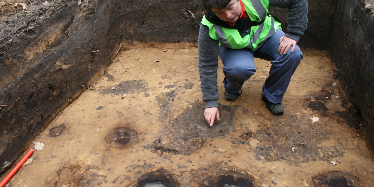Liesbeth Theunissen wijst in een werkput de sporen aan (bruin met grijze binnenkern) van twee palen uit de bronstijd.