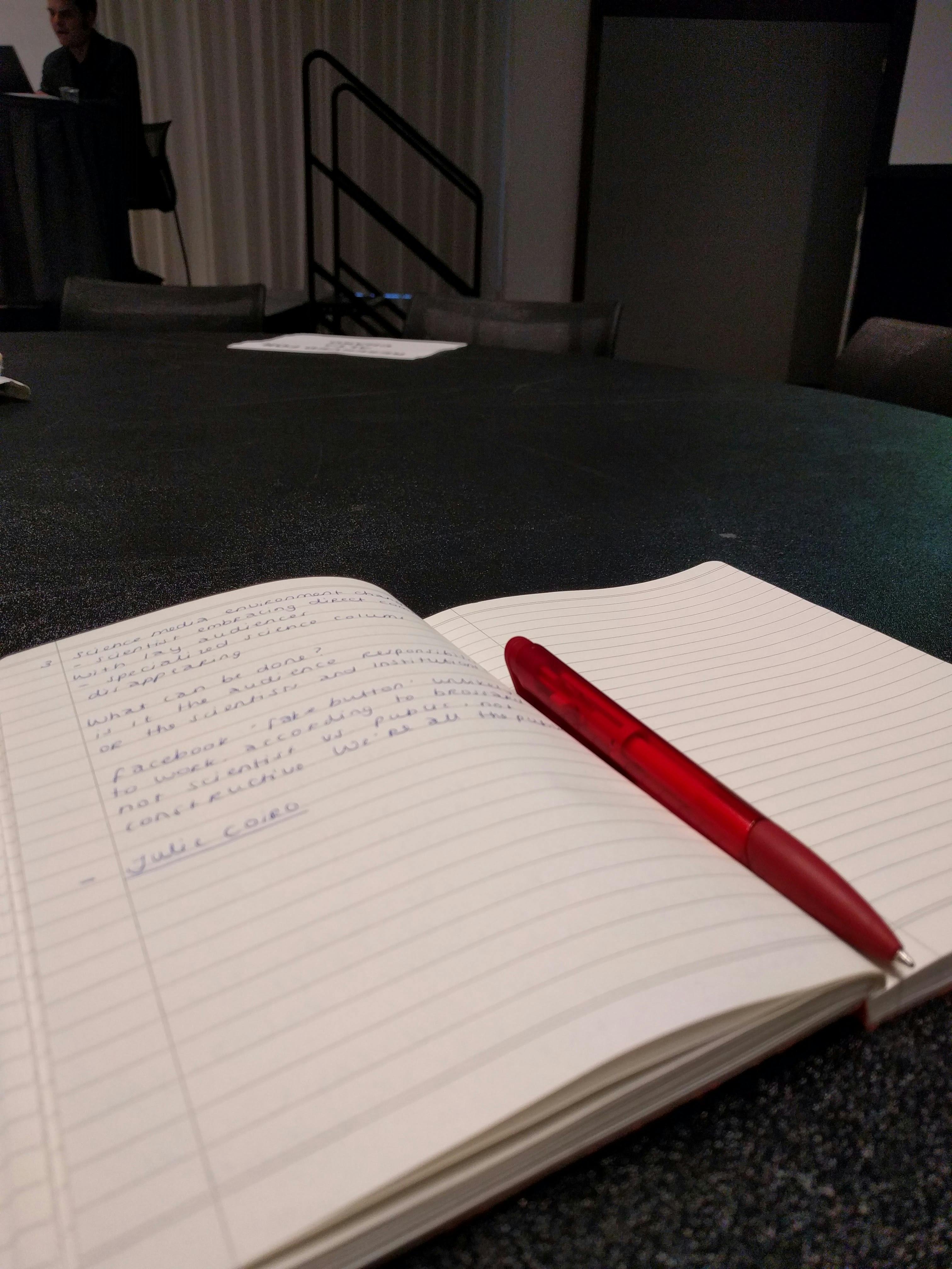 Een open notitieboekje op een tafel met een rode pen.