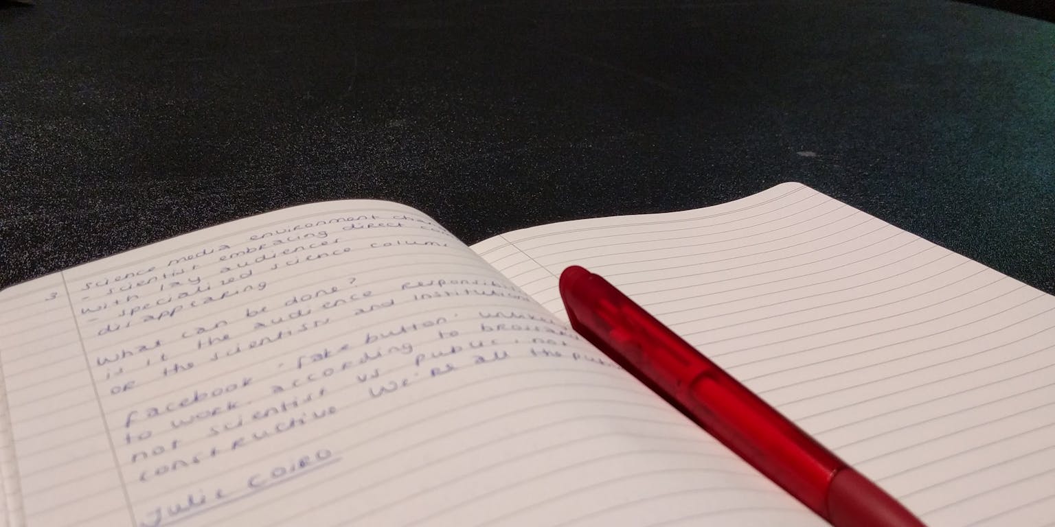 Een open notitieboekje op een tafel met een rode pen.