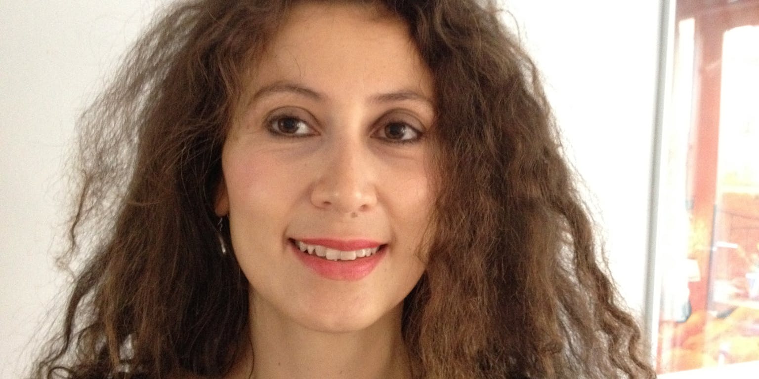 Een vrouw met krullend haar lacht naar de camera.