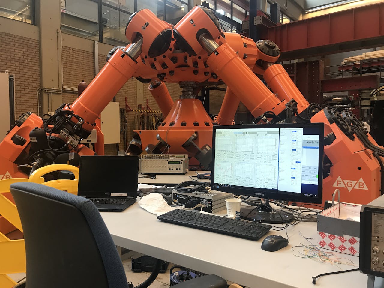 Het computerscherm geeft de meetgegevens weer en de hexapod schudt om de las in de buis (midden) te testen.