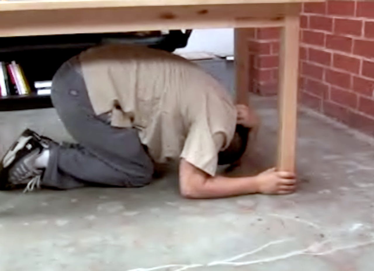 Een man geknield onder een houten tafel.