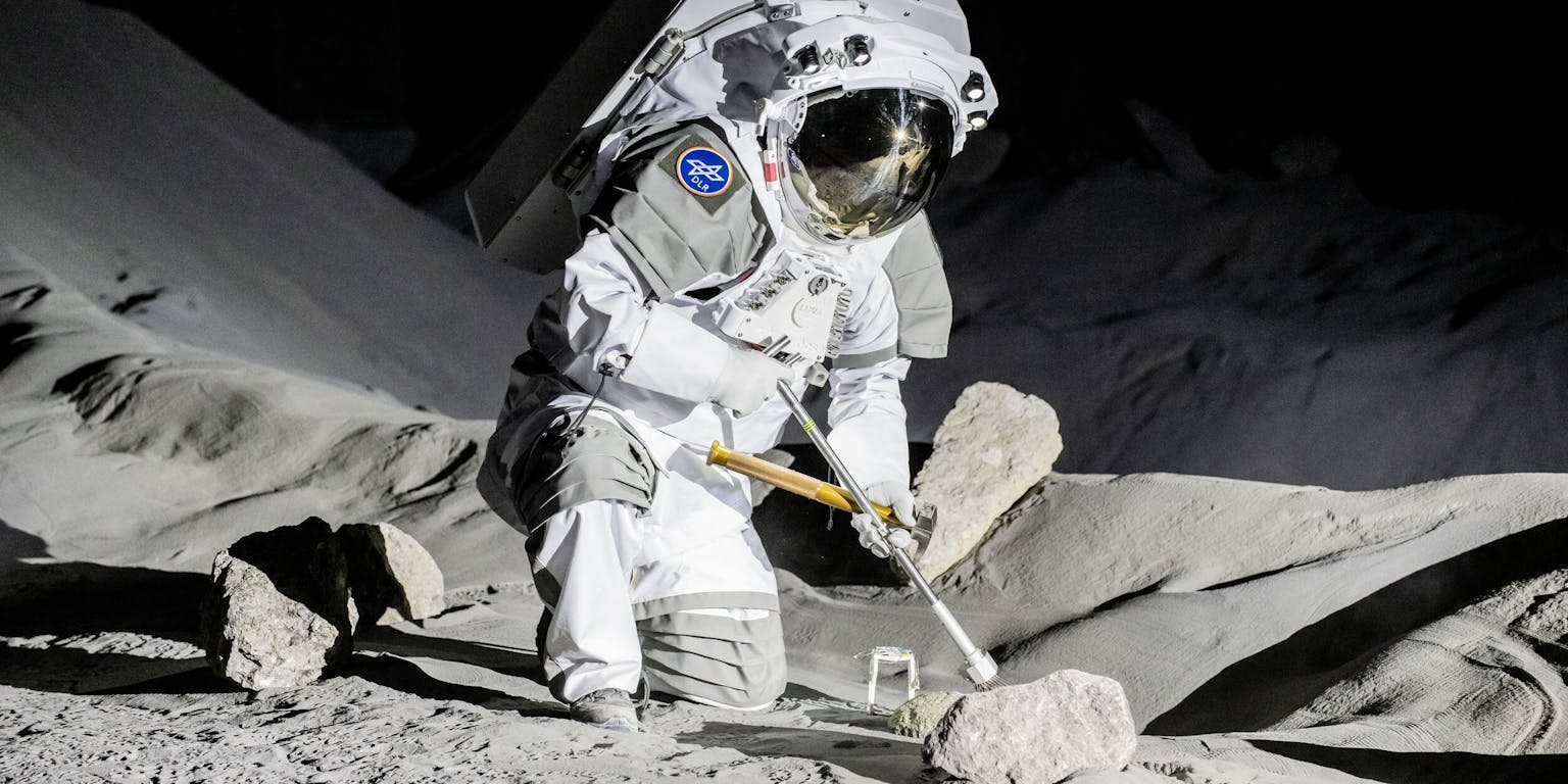 Een astronaut knielt in een grijs landschap en neemt met een instrument een bodemmonster.