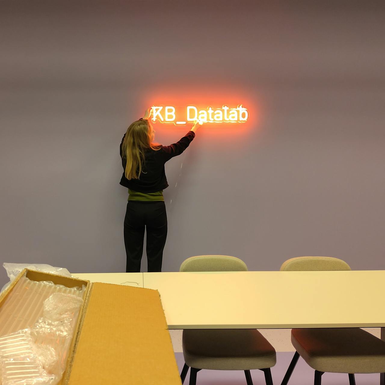 Een vrouw hangt het logo van het KB-Datalab in lichtgevende neonletters aan de muur.
