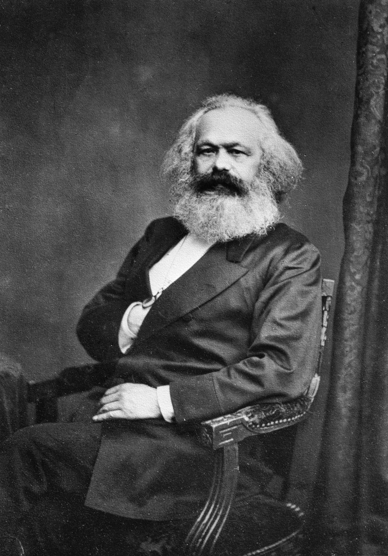 Een zwart-witfoto van Karl Marx zittend in een stoel.