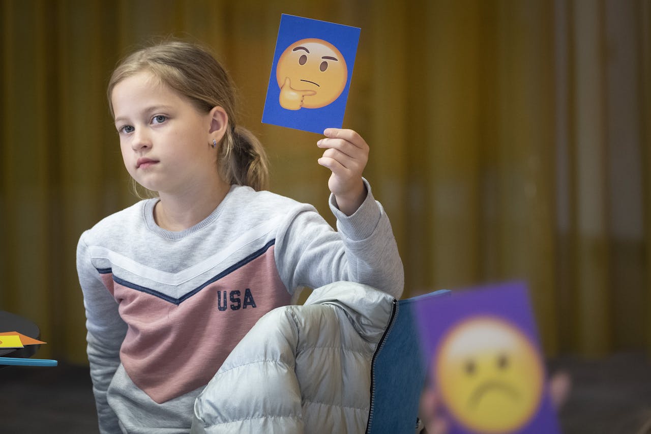 Een kind houdt een blauwe kaart omhoog. Op deze kaart staat een emoji die bedenkelijk kijkt.