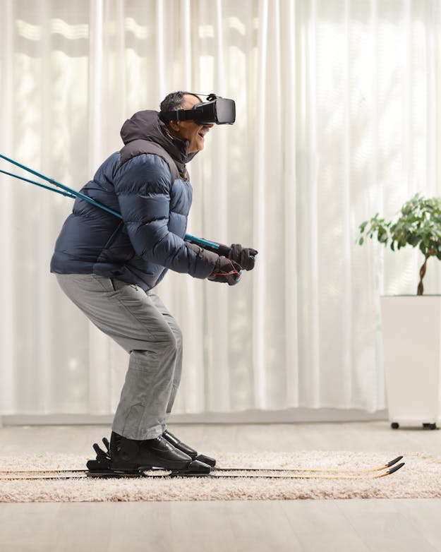 De berg af skiën zonder daarvoor naar buiten te hoeven: in virtual reality kan het. Oudere man in winterkleding op ski's in zijn woonkamer, met een VR-bril op