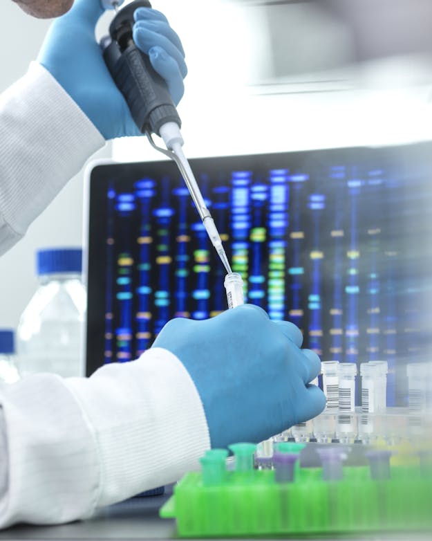 Genetische data zijn meestal geanonimiseerd en dus niet herleidbaar naar een persoon. Handen van een laborant die aan het pipeteren is, met op de achtergrond een beeldscherm met daarop een genoom