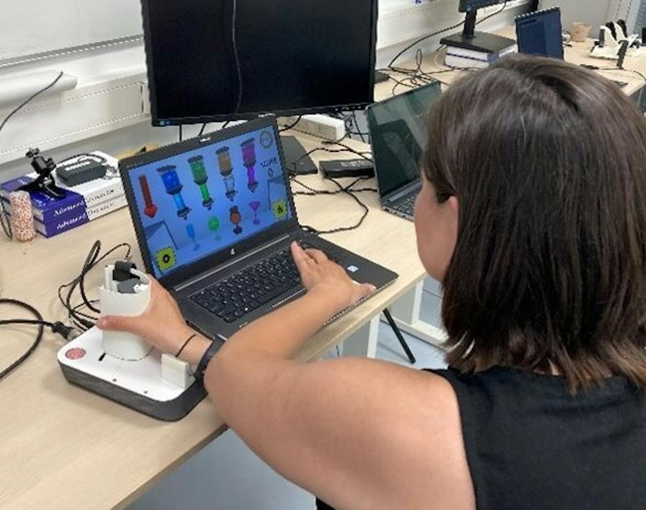 Laura Marchal-Crespo demonstreert de compacte versie van de Lambda 3+. Foto van ingenieur Laura Marchal-Crespo, die de compacte versie van de Lambda 3+ demonstreert. Zij zit achter een computerscherm, met haar rechterhand rond een witte plastic cilinder.