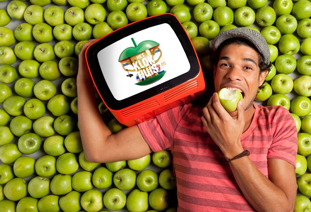 Een man die een tv vasthoudt voor een bos groene appels. Op het televisiescherm staat het logo van televisieprogramma het klokhuis.