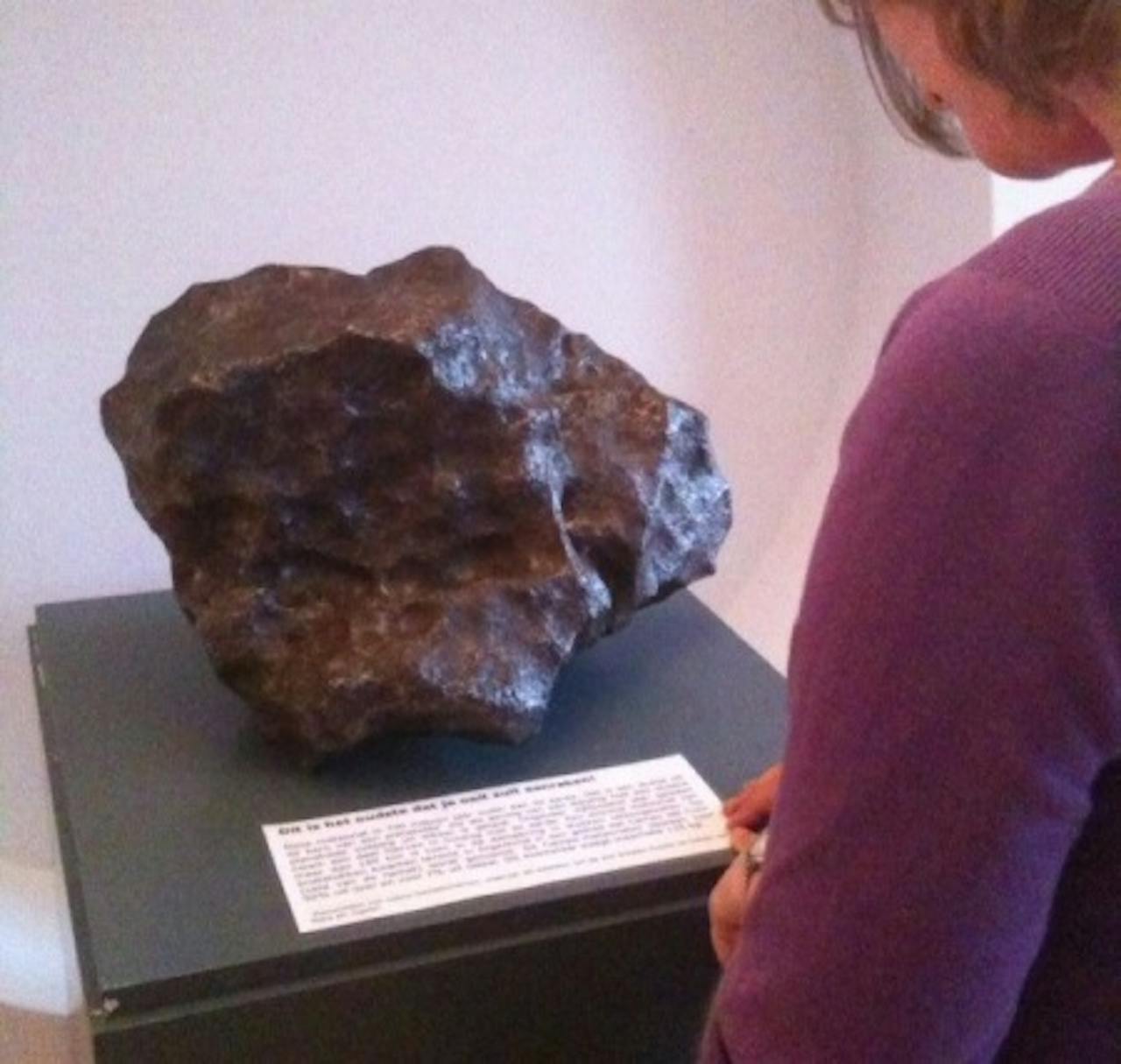 Een persoon kijkt naar een meteoriet die in een museum wordt tentoongesteld.