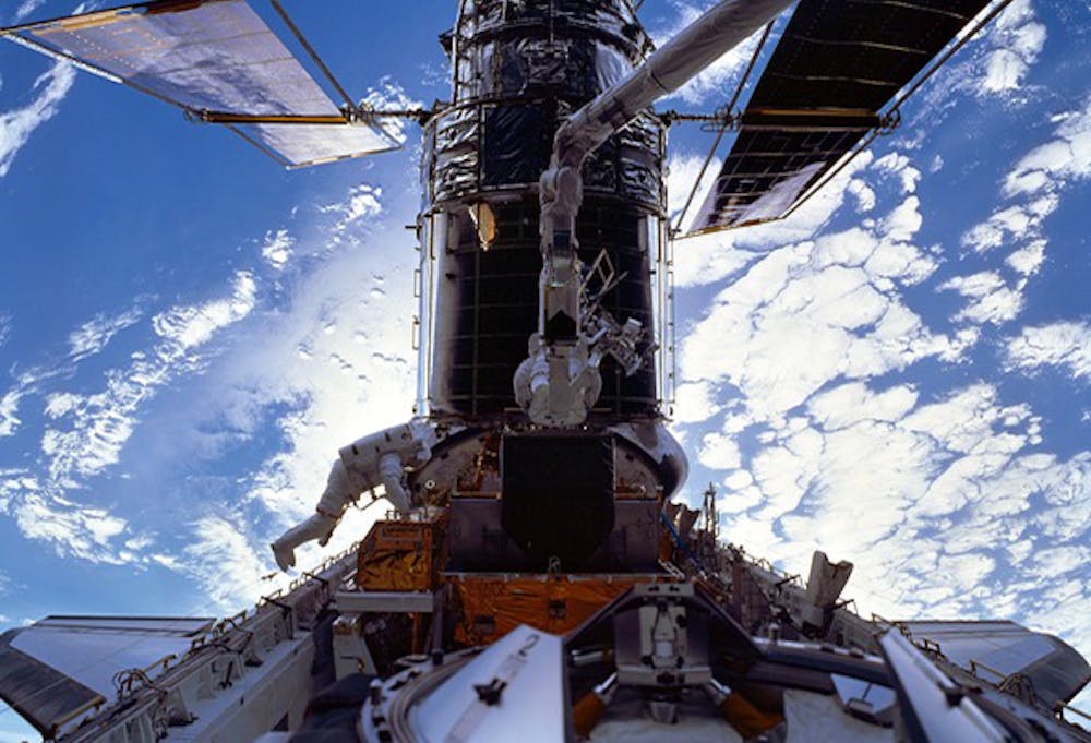 <p>De Hubble-telescoop gekoppeld aan de Spaceshuttle, tijdens een van de reparatiemissies. De Zwitserse astronaut Claude Nicollier is in het midden te zien, gekoppeld aan een robotarm.</p>
