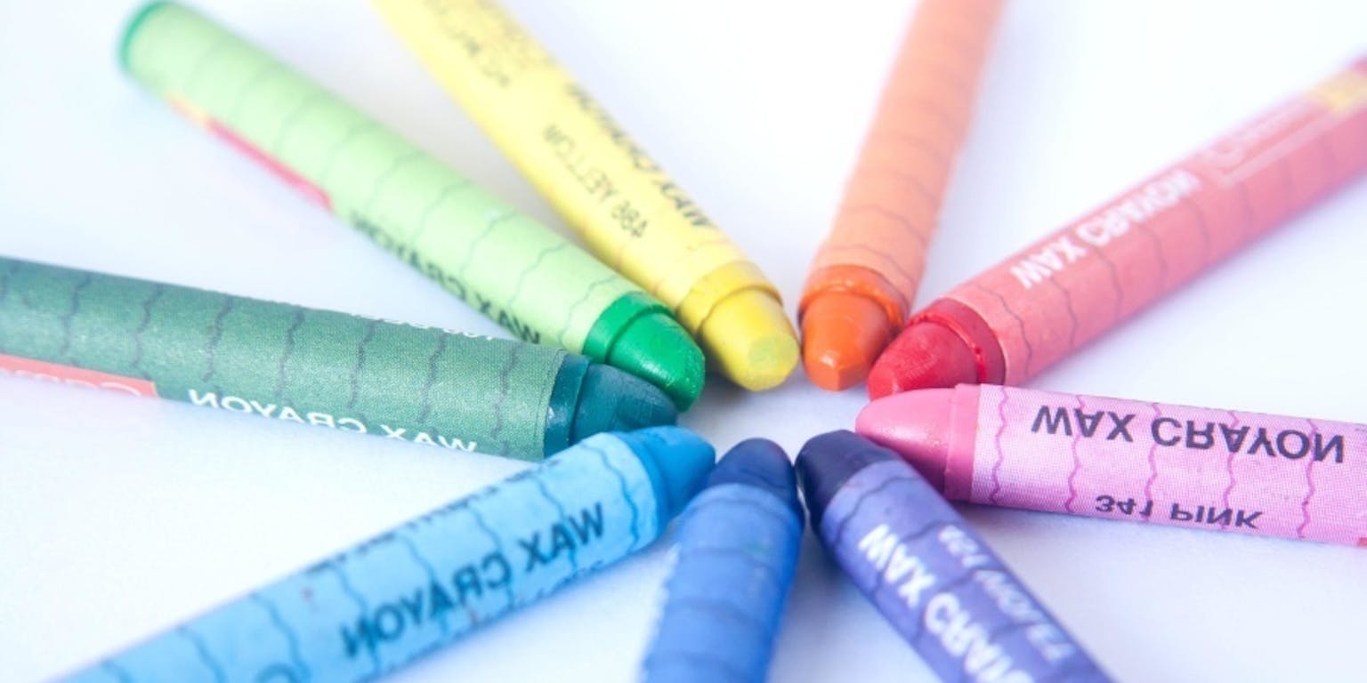 Kleurrijke waskrijtjes liggen in een cirkel op een witte ondergrond.