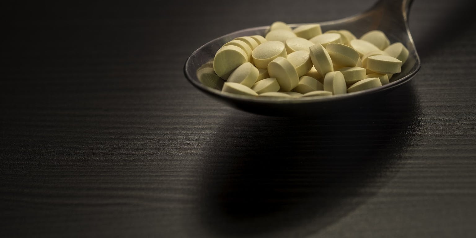 Een lepel vol pillen op een zwart oppervlak.