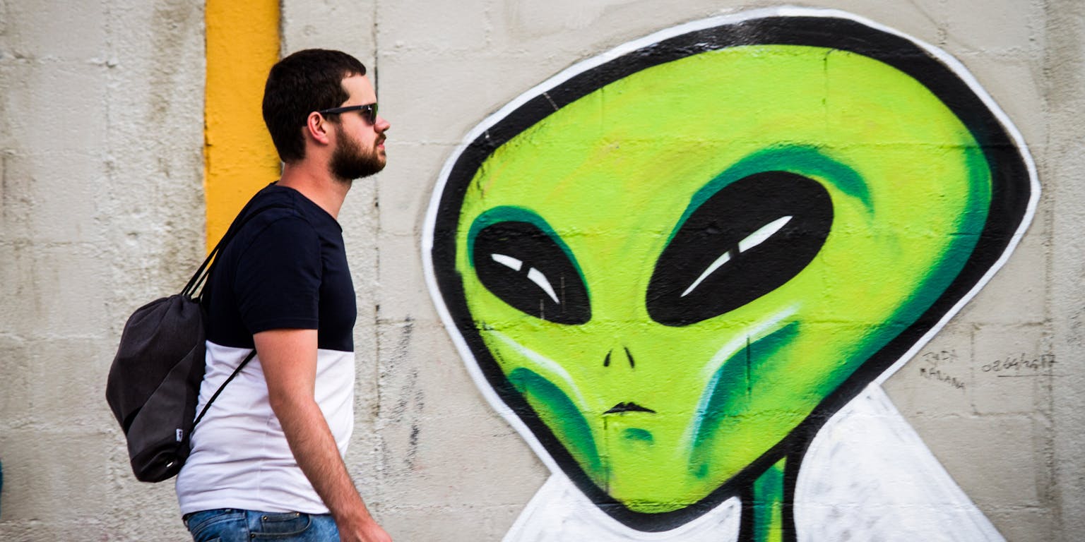 Een man kijkt naar een groene alien die op een muur is geschilderd.