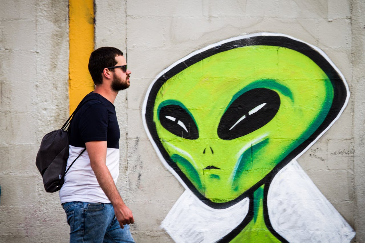 Een man kijkt naar een groene alien die op een muur is geschilderd.