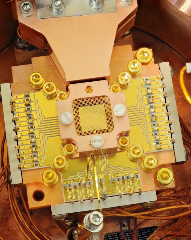 Quantum Computing; Ion Trapping processing in a quantum computer. The ions are trapped about 40 micrometers apart above the square gold chip in the center. The chip is surrounded by NIST physicists used this apparatus to coax two beryllium ions (electrically charged atoms) into swapping the smallest measurable units of energy back and forth, a technique that may simplify information processing in a quantum computer. The ions are trapped about 40 micrometers apart above the square gold chip in the center. The chip is surrounded by a copper enclosure and gold wire mesh to prevent buildup of static charge.