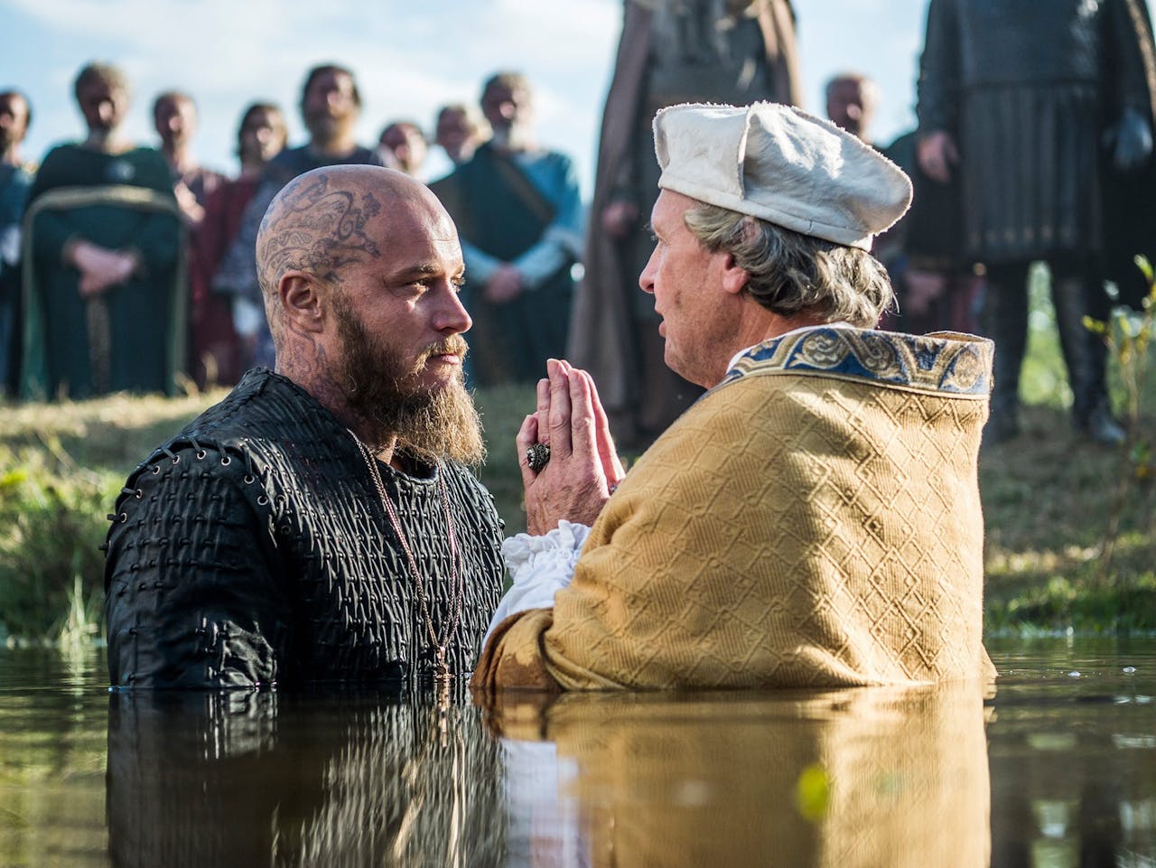 Ragnar laat zich dopen in Vikings. De twee personages staan tot diep in het water.