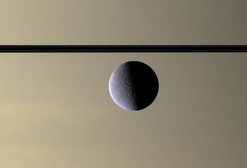 <p>De maan Rhea voor Saturnus haar ringen (van opzij gezien). De foto werd in 2007 door ruimtesonde Cassini gemaakt. Rhea heeft een diameter van 1527 kilometer en is na Titan de grootste maan van Saturnus.</p>