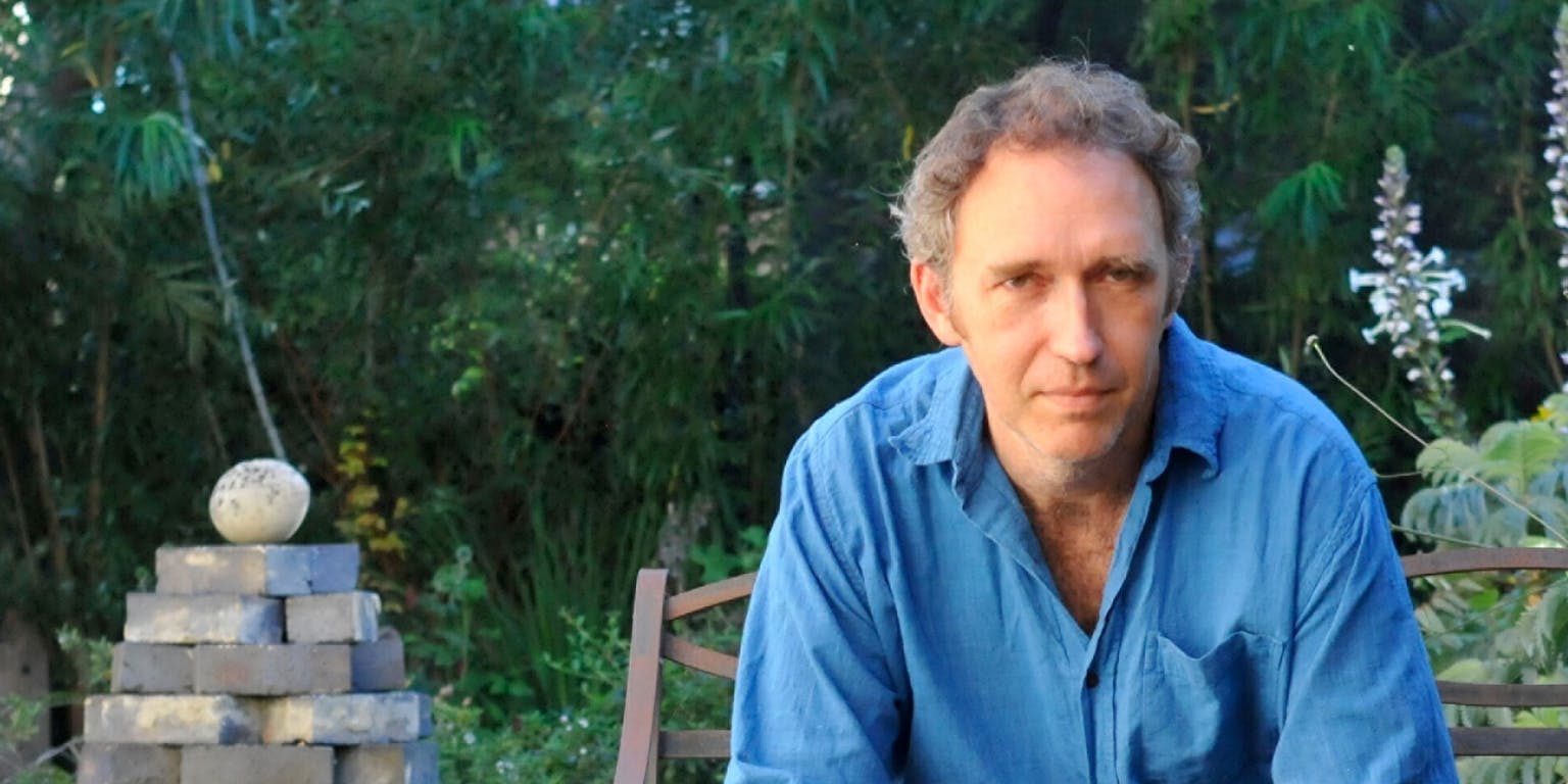 Een man in een blauw shirt zit op een stoel voor een stapel stenen.