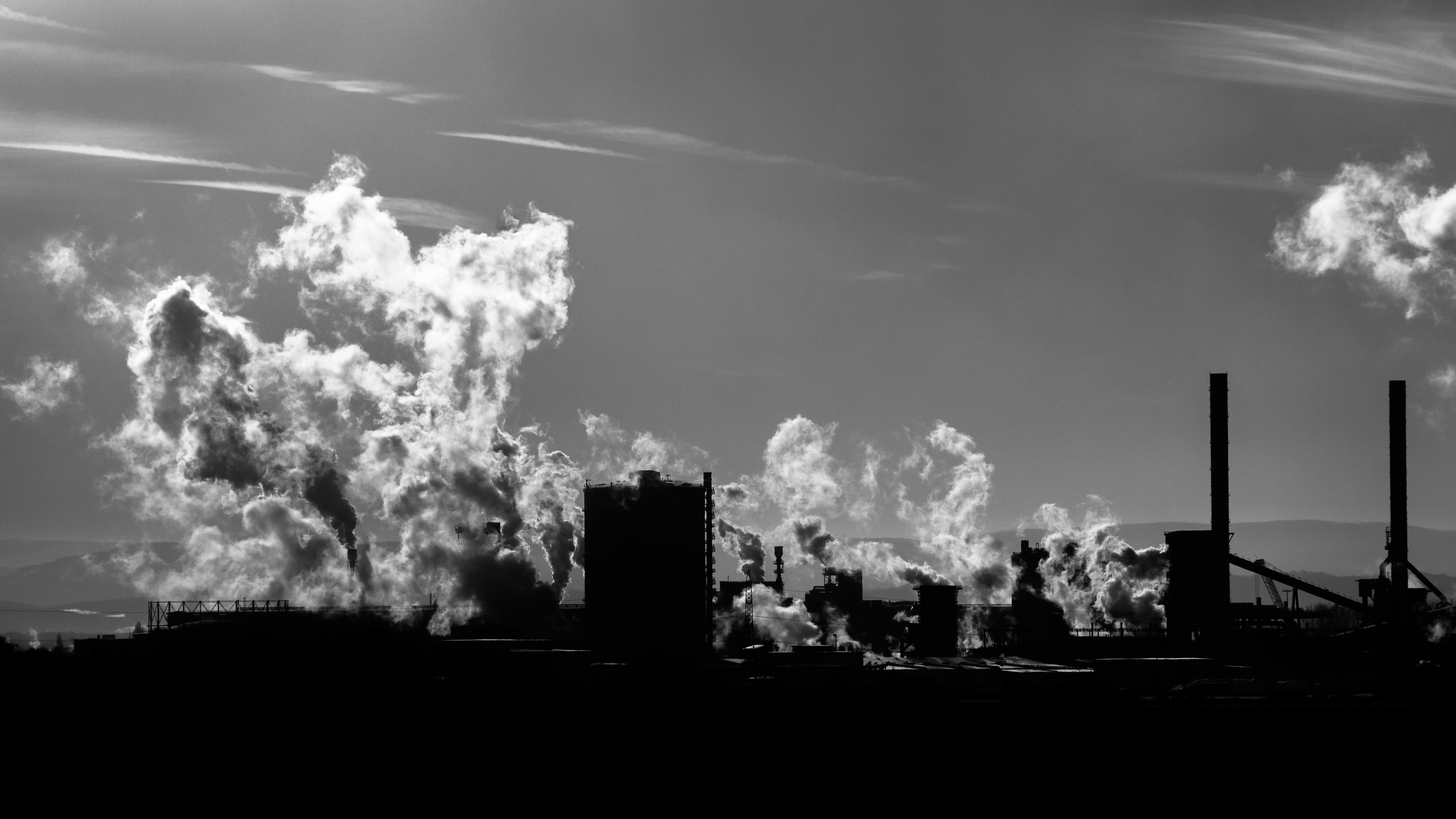 Een zwart-wit foto van een staalfabriek in Salzgitter, Duitsland. Er komt rook uit de fabriek.