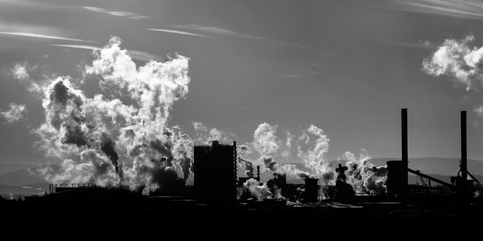 Een zwart-wit foto van een staalfabriek in Salzgitter, Duitsland. Er komt rook uit de fabriek.