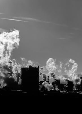 Een zwart-wit foto van een staalfabriek in Salzgitter, Duitsland. Er komt rook uit de fabriek.