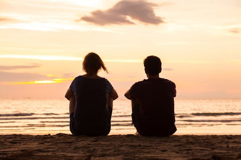 Als je er samen niet uitkomt, laat het dan met rust en richt je op de dingen die jullie wél delen, adviseren experts Een man en een vrouw op de rug gezien, zittend op het strand tijdens een zonsondergang