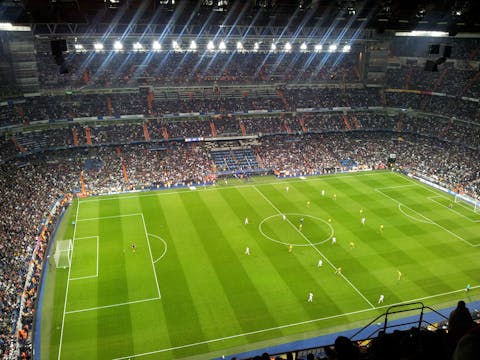 In Bernabéu, het station van Real Madrid, ligt Barenbrug-gras. Voetbalstadion met spelers op het veld en gevulde tribunes. De verlichting is aan.