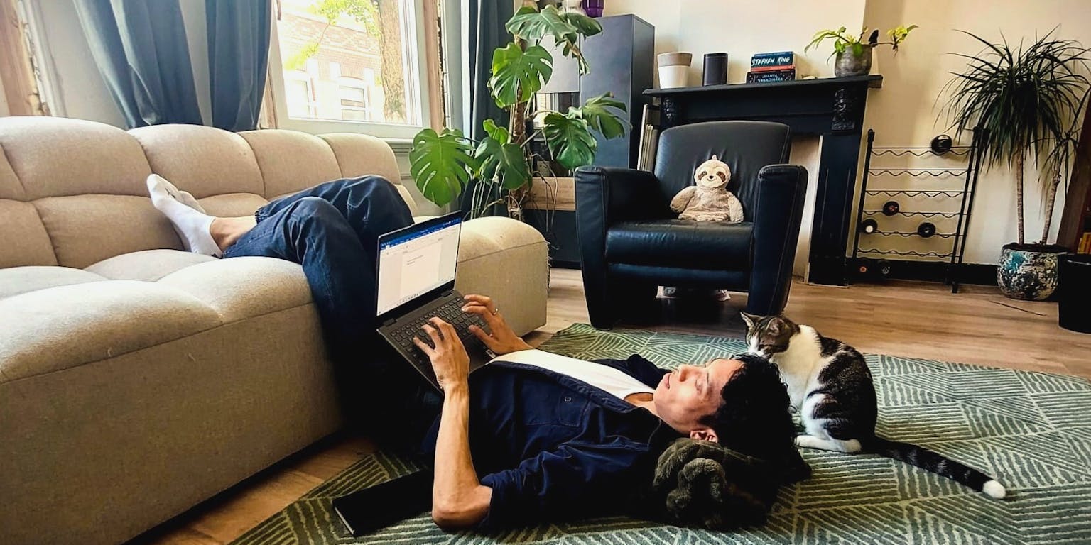 Face of Science Patrick Tang schrijft ondersteboven hangend op zijn bank een wetenschappelijk artikel op zijn laptop, terwijl zijn kat toekijkt