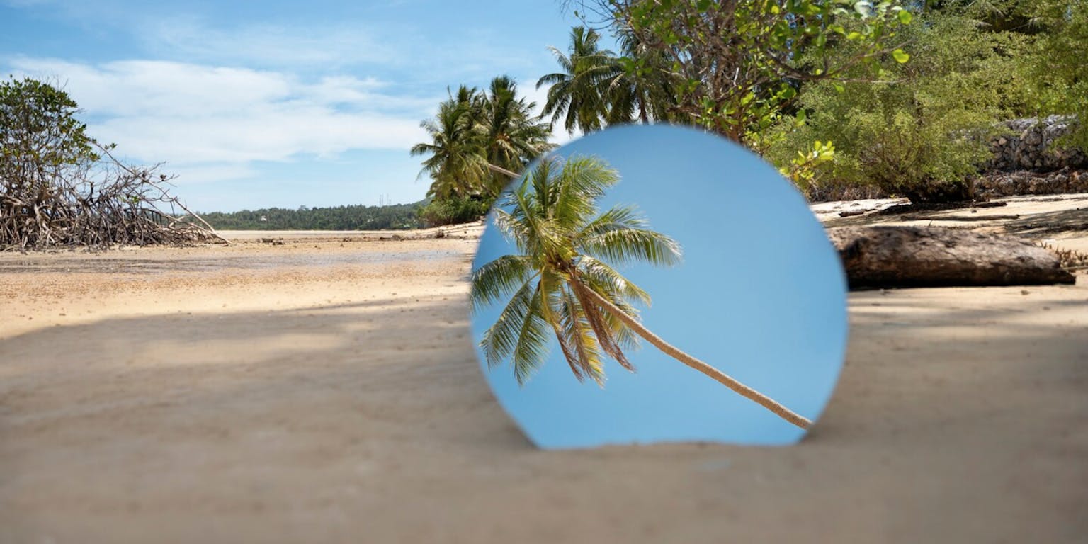 een tropisch strand met palmbomen met de weerspiegeling van een palmboom in een spiegel gevangen