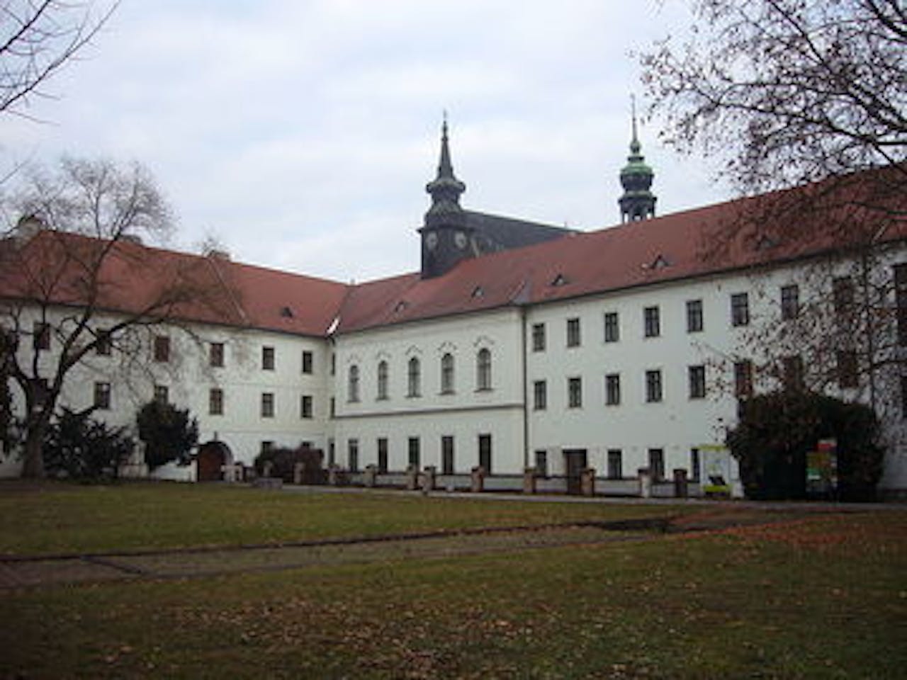 Een klooster met witte muren, een grasveld en twee kerktorens.