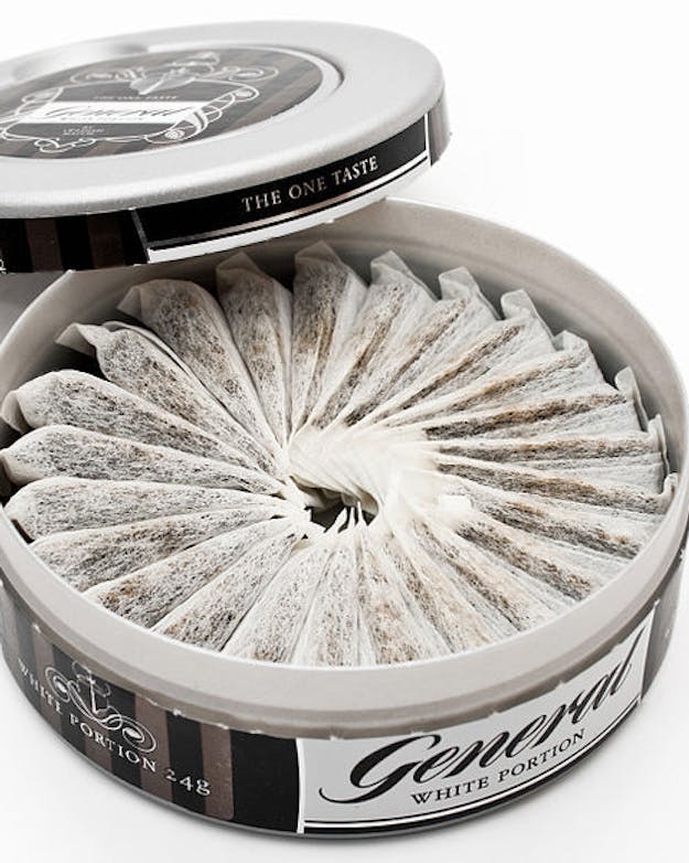 Snus zit in een soort theezakjes en bevat nicotine en smaakjes in poedervorm. De zakjes stop je tussen je lip en je tandvlees, waar vervolgens de nicotine in de bloedbaan terechtkomt. Foto van een rond blikje met daarin zakjes snus