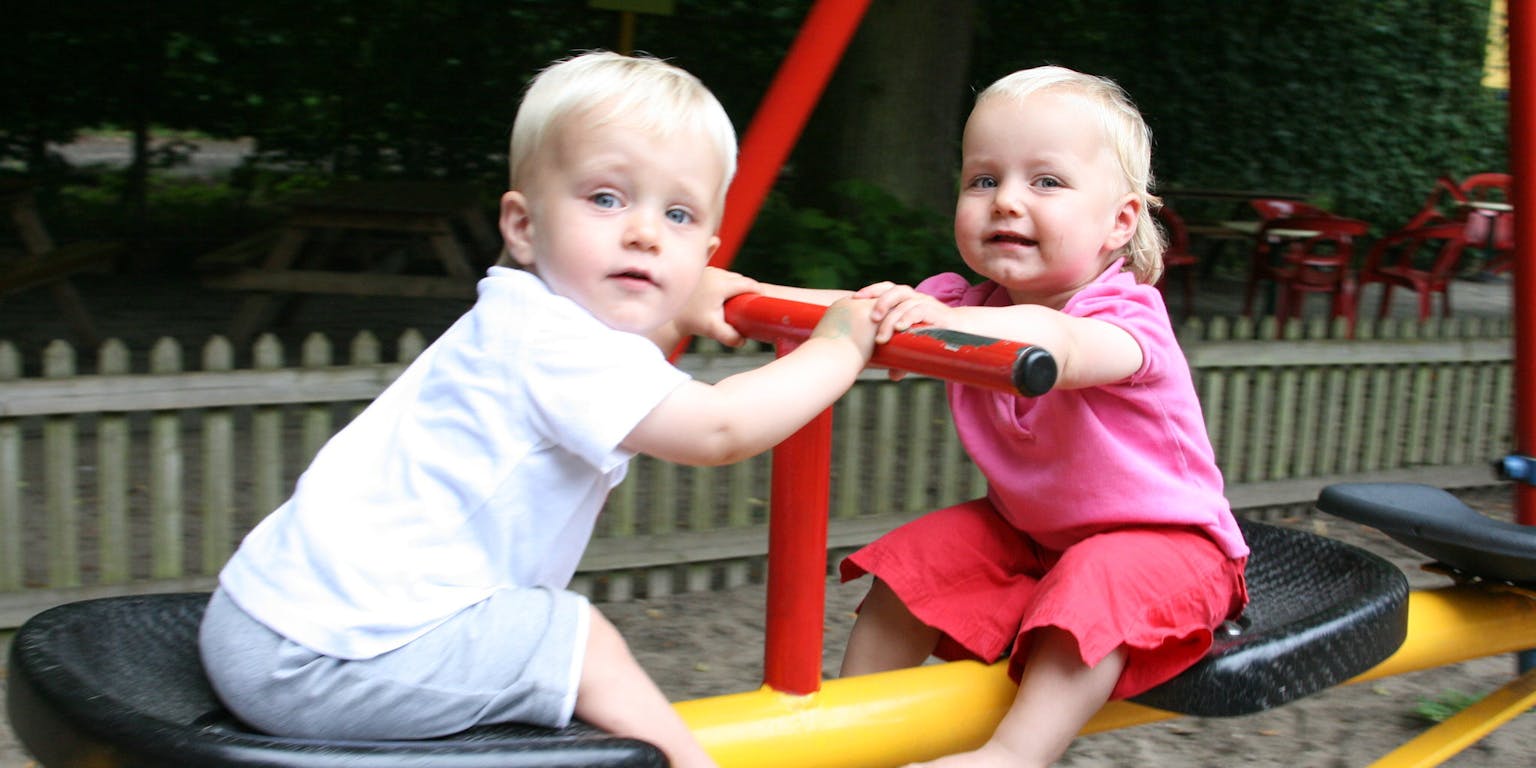 Twee kleine kinderen spelen op een speelplaats.